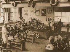 an old black and white photo of people looking at motorcycles in a garage with men working on them