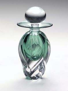 a green glass bottle with a silver top on a white surface, in the shape of an object