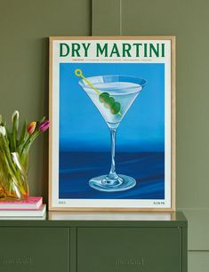 a martini glass with green olives in it on a shelf next to a vase filled with tulips