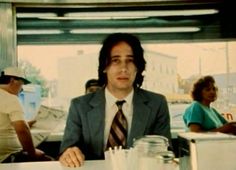 a man in a suit and tie sitting at a table with other people behind him