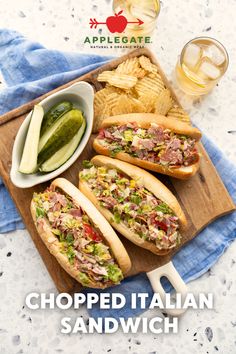 two sandwiches with pickles and chips on a cutting board next to a glass of beer