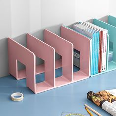 three pink bookshelves sitting next to each other on a blue table with pens and pencils