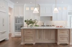 a large kitchen with white cabinets and wooden flooring, along with an island in the middle