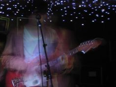 a man with a red guitar in front of a microphone and some lights on the wall