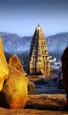 an ancient temple with large rocks in the foreground and mountains in the back ground