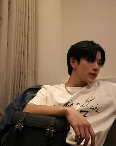 a young man sitting in a chair holding a black bag and looking off to the side