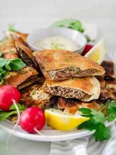 a white plate topped with quesadillas covered in meat and vegetables next to lemon wedges