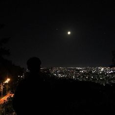 a man standing on top of a hill looking at the city lights in the distance