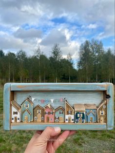 a hand holding up a small wooden box with houses in it