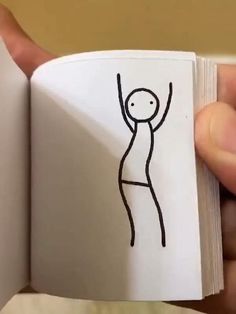 a hand holding an open book with a drawing of a person on the inside of it