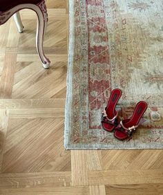 a pair of red shoes sitting on top of a wooden floor next to a rug