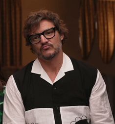 a man with glasses is sitting down and looking at the camera while wearing a black and white shirt