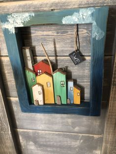 a small wooden frame with houses painted on it and a tag hanging from the front