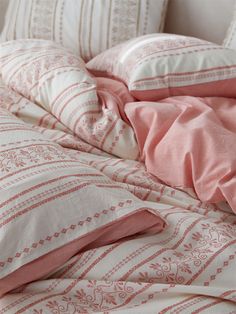 an unmade bed with pink and white sheets, pillows and blankets on top of it