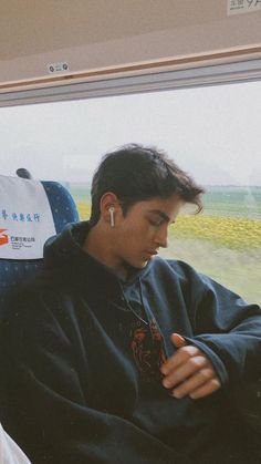 a young man sitting on a train looking at his cell phone while wearing ear buds