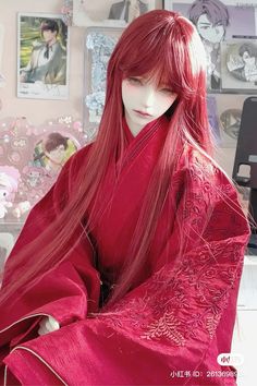 a woman with long red hair wearing a kimono in front of a desk and pictures on the wall behind her