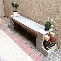 a concrete bench with potted plants on it next to a wall and brick walkway