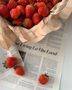 a bunch of strawberries sitting in a paper bag on top of a news paper