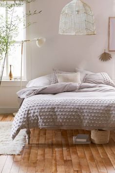 a white bed sitting on top of a hard wood floor next to a potted plant