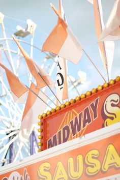 the midway sign has flags flying from it's sides and on top of it is a ferris wheel