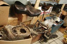 an old motorcycle in a garage with other parts on the floor and boxes around it