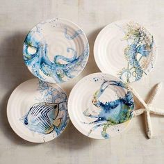 four plates with sea animals painted on them next to starfish and seashells