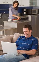 a man sitting on a couch with a laptop computer in his hand and a woman standing behind him