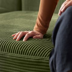 a person sitting on a green couch with their hand resting on the armrests