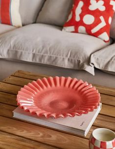 a red plate sitting on top of a wooden table next to a cup and saucer