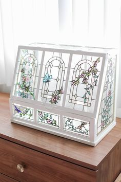 a stained glass box sitting on top of a wooden table next to a white window