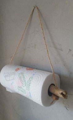 a roll of toilet paper hanging from a rope on the wall with a wooden stick attached to it