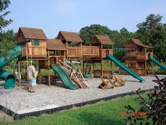 a man standing in front of a wooden playground structure with slides and climbing equipment on it