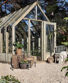 a wooden greenhouse with glass walls and plants in the front, sitting on gravel ground