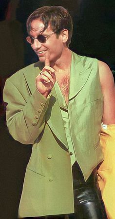 a man in a green jacket and black pants is holding his hand to his mouth