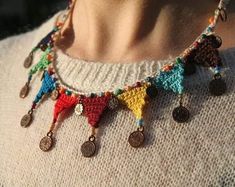 a woman wearing a multicolored crocheted necklace with coins hanging from it