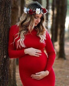 a pregnant woman in a red dress standing next to a tree wearing a flower crown