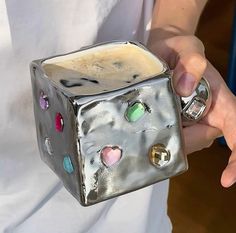 a person is holding a silver cube shaped mug with hearts on the outside and inside