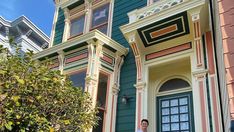 a man standing in front of a green and yellow house with blue trimmings