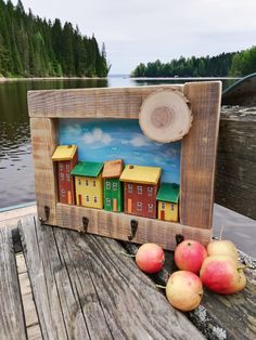 some apples are sitting on a wooden table next to a picture frame with houses painted on it