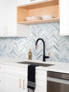 a kitchen with white cabinets and marble backsplash, brass faucet, black towel hanging from the sink