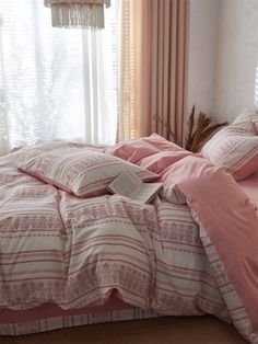 a bed with pink comforters and pillows in a room next to a white window