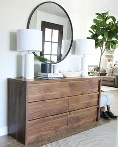 a dresser with a mirror, lamp and plant on it in a living room area