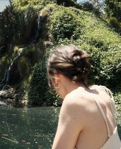 a woman standing in front of a waterfall with her back to the camera and looking at it