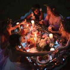 a group of people sitting around a table with food and candles in the shape of flowers