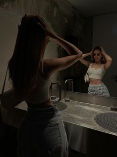 a woman standing in front of a bathroom sink with her hands on her head and looking at herself in the mirror