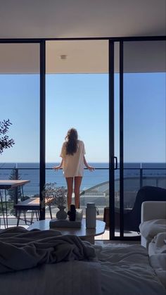 a woman standing in front of an open door looking out at the ocean from her bedroom