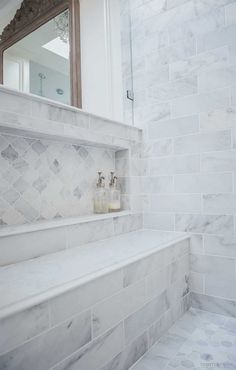 a bathroom with white marble walls and flooring next to a mirror on the wall