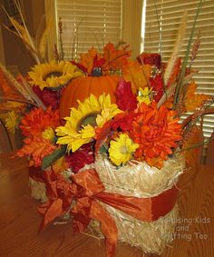 an arrangement of fall flowers and pumpkins in a basket on a dining room table