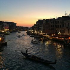 a boat traveling down a river next to tall buildings at dusk with the sun setting