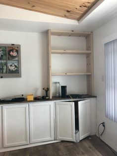 a kitchen with white cabinets and wood flooring next to a wall mounted book shelf